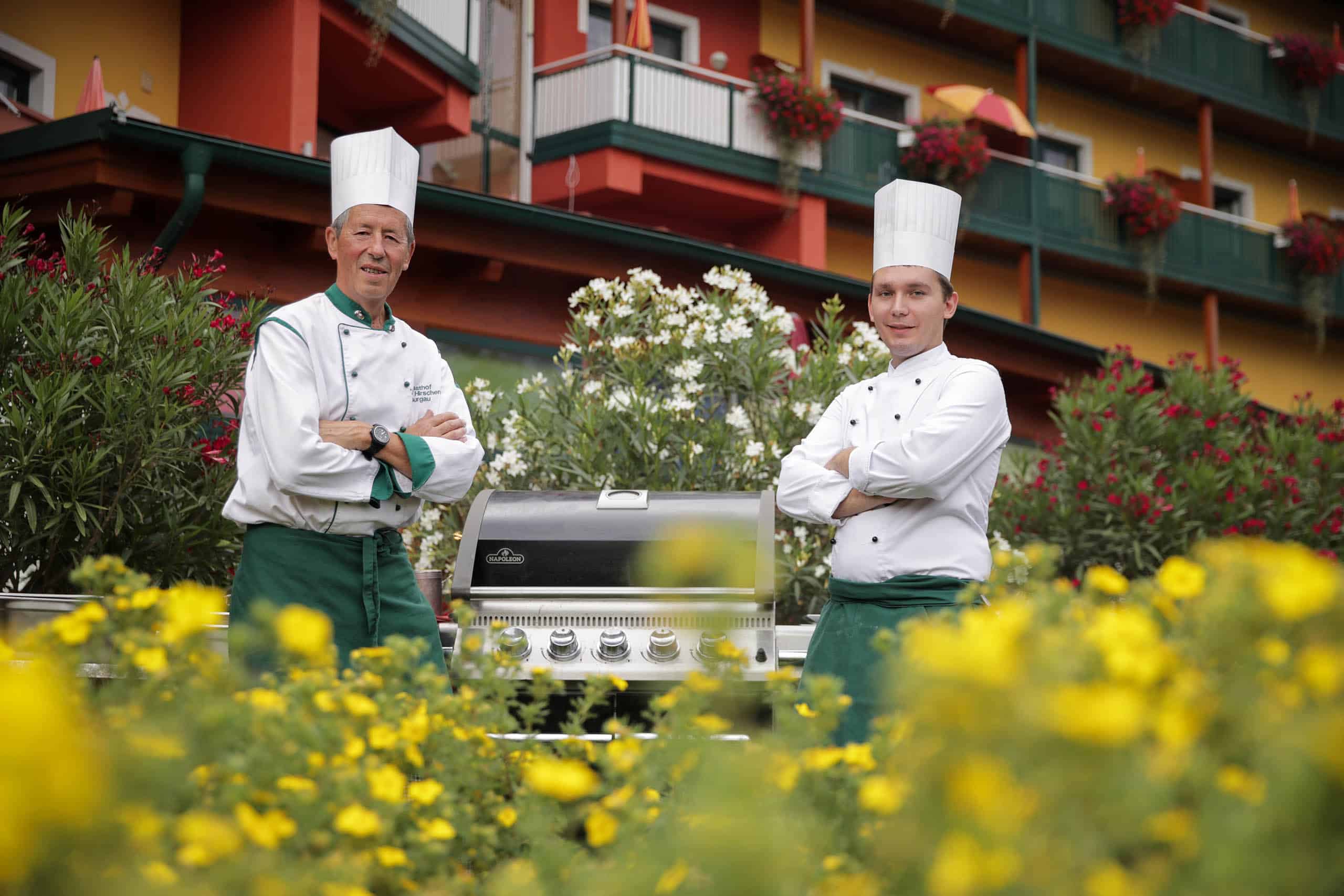 PuchasPLUS Köche inmitten schöner Blumen vor dem Thermenhotel beim Grillen.